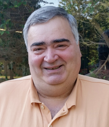 A man with salt and pepper hair and wearing an orange shirt smiles at the camera.