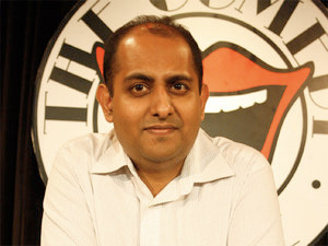 A balding South Asian man in a white collar shirt looks at the camera.