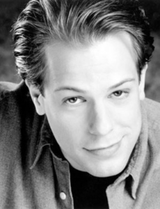 A grayscale portrait of a young man who smirks up into the camera.