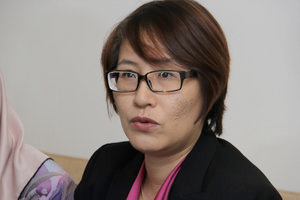 A woman with dark hair and black rectangular glasses speaks to someone to the left of the photographer.