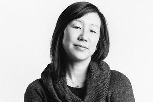 A grayscale portrait of an East Asian woman with shoulder-length hair wearing a dark hoodie. 
