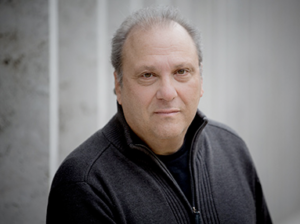 A balding middle aged man in a black quarter-zip looks seriously at the camera.