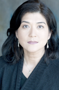 A woman with light skin and very dark hair wears silver drop earrings and a black V-neck blouse.