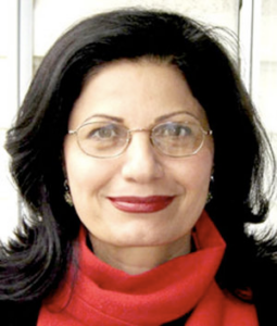 A light skinned woman with dark hair wearing oval glasses and a red turtleneck smiles at the camera.