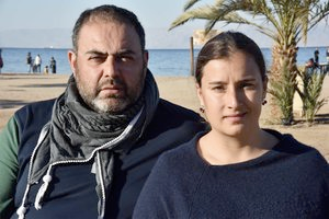 A man and a woman look into the camera. The man has a short beard and is wearing a gray scarf. The woman has her hair pulled back and is wearing a navy top.