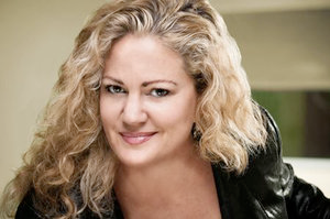 A blonde woman with curly hair smiles into the camera