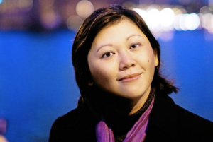 An asian woman with shoulder length hair and a purple scarf smiles at the camera