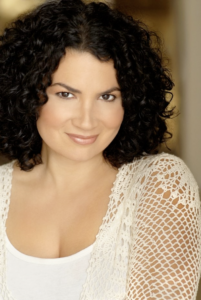 A light skinned woman with dark curly hair smiles into the camera. 