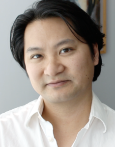 A man wearing a white shirt looks into the camera.