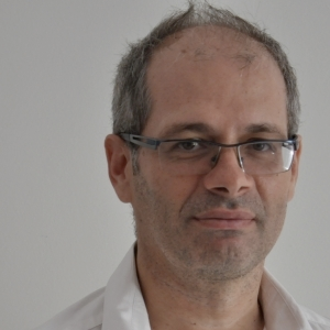 A man with thinning salt-and-pepper hair wearing rimless glasses looks at the camera.