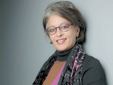 A three-quarter portrait of a woman with salt-and-pepper hair and wearing cat-eye purple glasses.