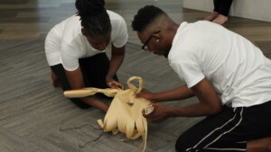 Two people in white T-shirts hold a white prop while kneeling on the floor.