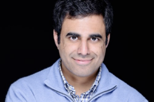 A man with heavy black eyebrows looks directly at the camera.