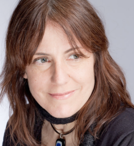 A light-skinned woman with reddish-brown hair and hazel eyes looks to the right of the camera.