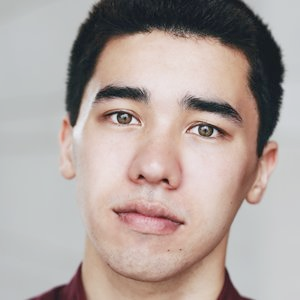 A serious young man with black hair and hazel eyes looks into the camera. 