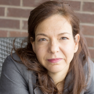 A light-skinned woman with medium-brown hair smiles at the camera.