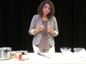A woman with curly brown hair cooks at a white table.